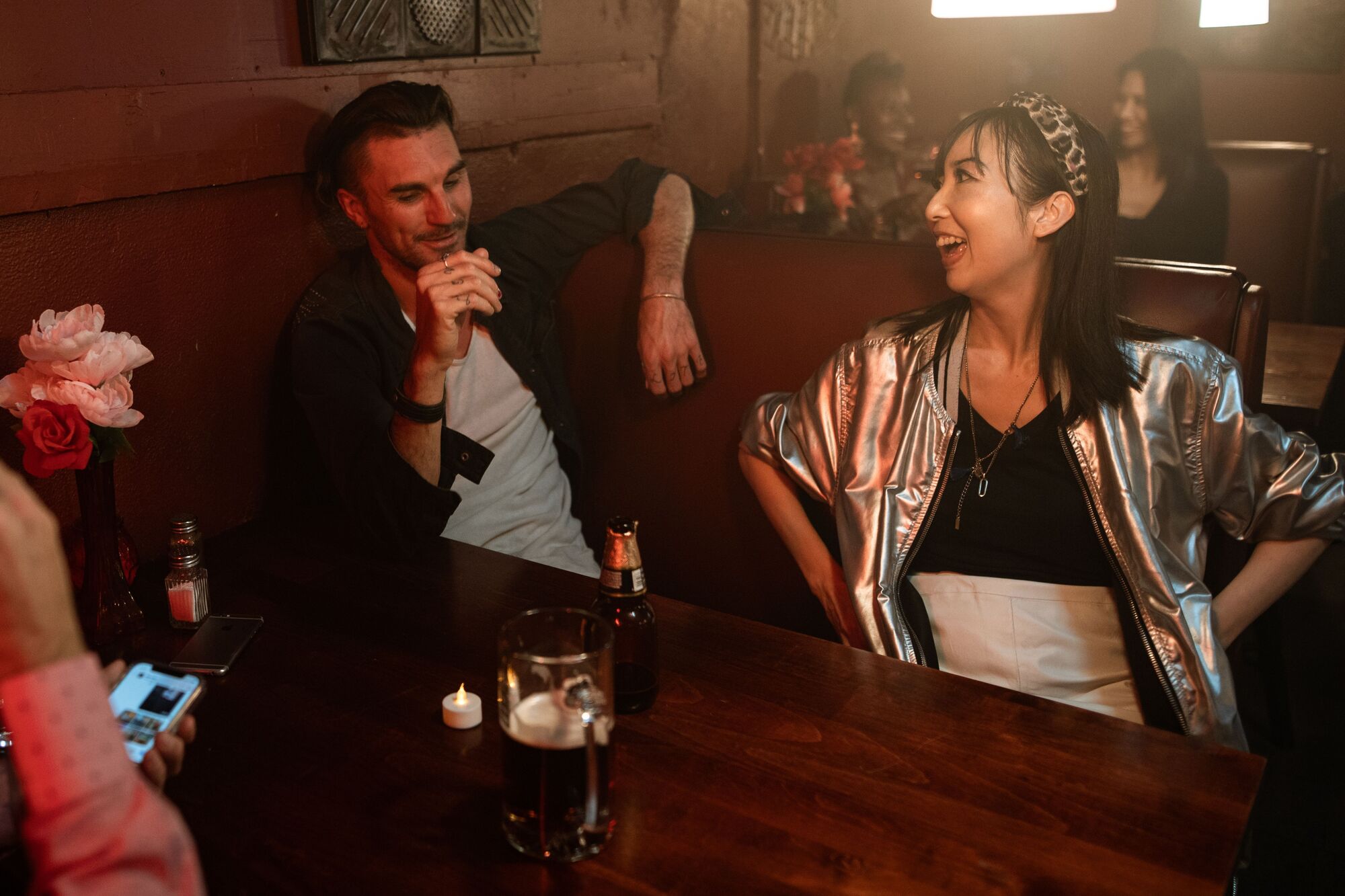 Two people in a warm bar booth laughing together over drinks