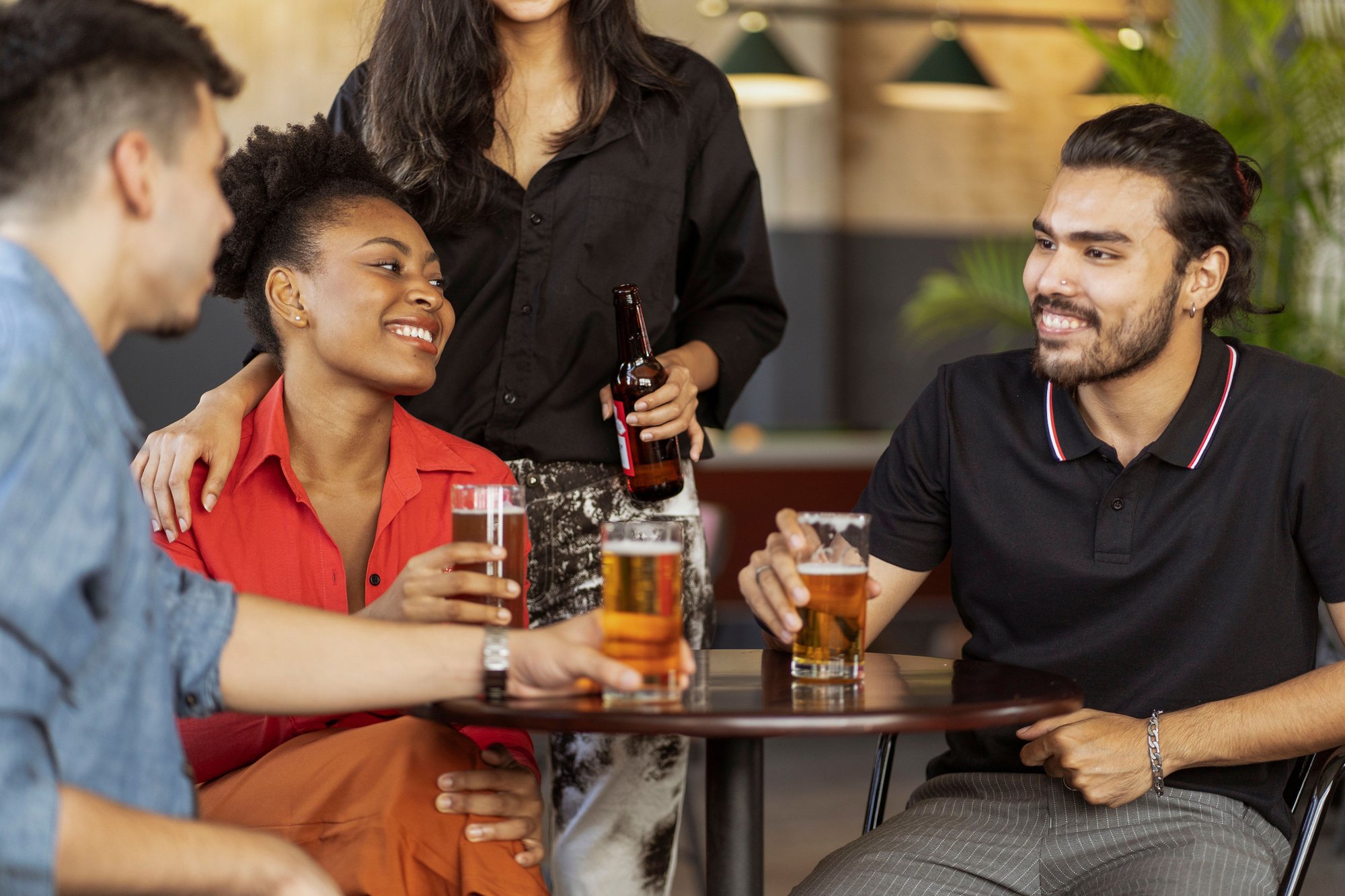 A mixed group of women and men laughing over drinks around a bar table